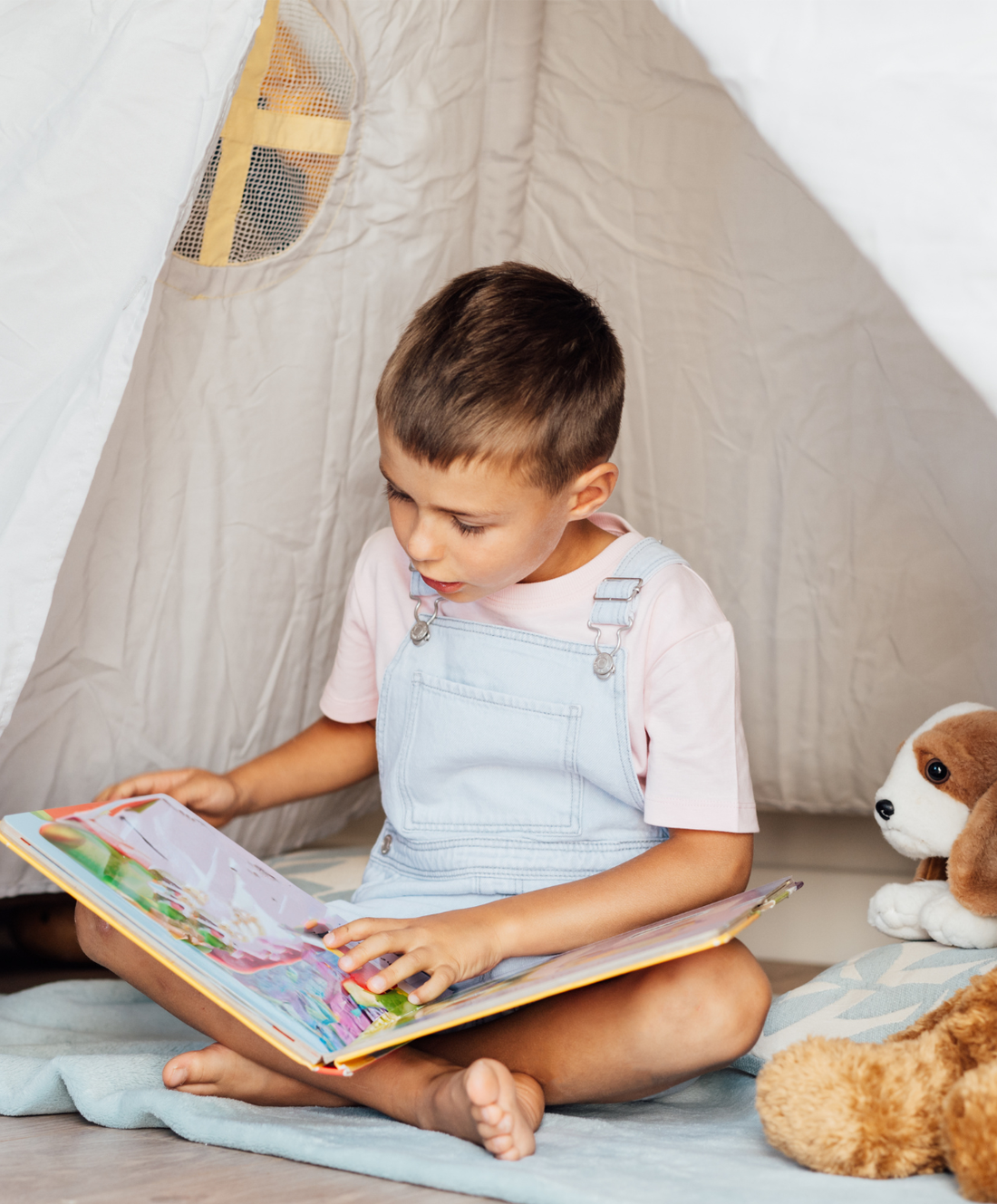 Boy reading a book in tent with stuffies